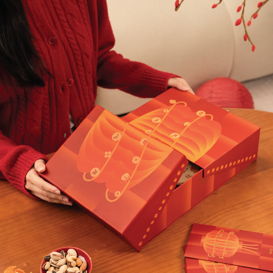 Person holding a red jewelry box with intricate designs on a wooden table.