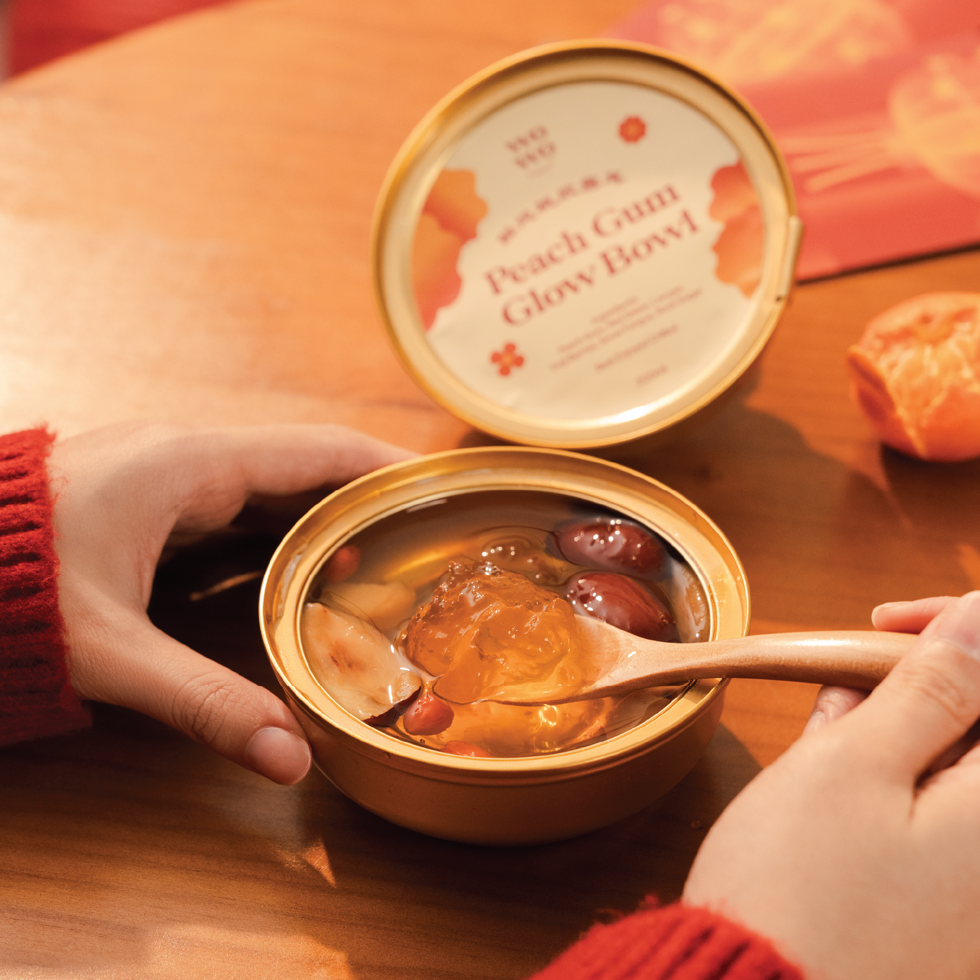 Person holding a container of peach gum glow bowl with a spoon inside, on a wooden table.