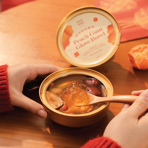 Person holding a container of peach gum glow bowl with a spoon inside, on a wooden table.